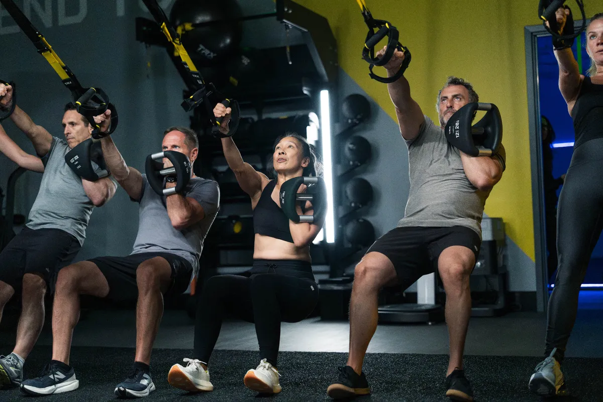 Members squatting with TRX straps and weights during a Check Fitness class