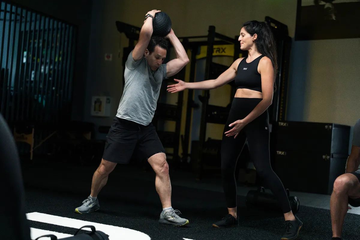 A coach guiding a member through an overhead slam ball during a Metcon class